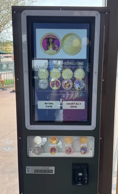 A Disney medallion machine: a touchscreen showing EPCOT and Disney Princess coins and offering Collectible Medallions at $10 each or 4 for $35, a display window of sample coins in clear cases, and a tap-to-pay card reader
